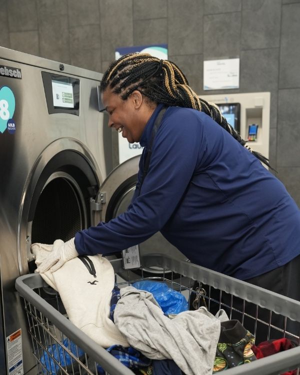 Woman loading laundry into a commercial washing machine at Luv Laundromat, showcasing the care and attention given to garments during the laundry process.